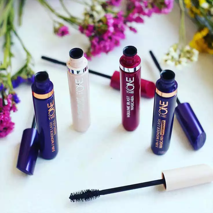 مجموعهای از ریملهای رنگی با برچسب «The One» روی یک سطح سفید چیده شدهاند. این ریملها در رنگهای بنفش، قرمز و بژ هستند و برخی از آنها باز هستند تا ریملها دیده شوند. در پسزمینه، گلهای محو شدهای با رنگهای مختلف وجود دارد که جلوهای پر جنب و جوش به تصویر میبخشد.